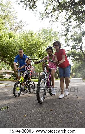Stock Photography - Parents helping children to ride bicycles on the road. Fotosearch