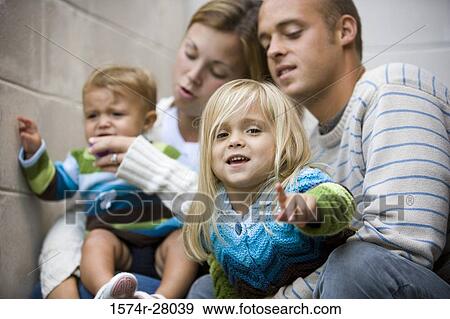 Parents sitting with their children by wall View Large Photo Image Stock Photo - Parents sitting with their children by wall. Fotosearch