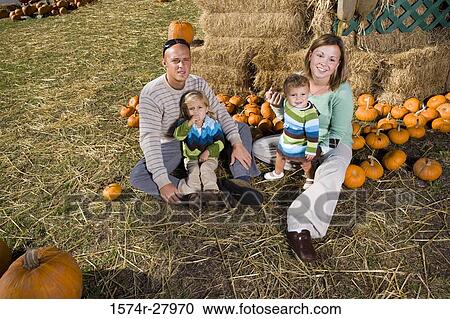 Stock Image - Parents with their children sitting by straw bundle. Fotosearch