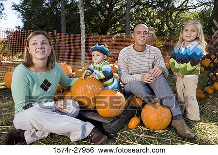 Parents with their children sitting amid pumpkins View Large Photo Image Stock Photograph - Parents with their children sitting amid pumpkins. Fotosearch