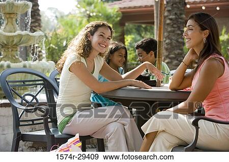 Stock Photo - People sitting together on chairs by table. Fotosearch