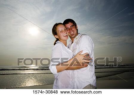 Portrait a cheerful young couple embracing on the beach View Large Photo Image Stock Photo - Portrait a cheerful young couple embracing on the beach. Fotosearch