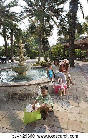 Portrait of a boy sitting with shopping bag while young women sitting with girl by water fountain View Large Photo Image Stock Image - Portrait of a boy sitting with shopping bag while young women sitting with girl by water fountain. Fotosearch