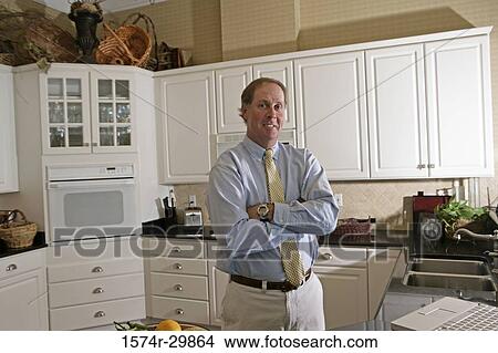 Picture - Portrait of a businessman standing in kitchen with his arms crossed. Fotosearch
