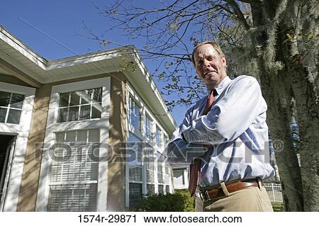 Stock Image - Portrait of a businessman standing with his arms crossed with a building in the background. Fotosearch