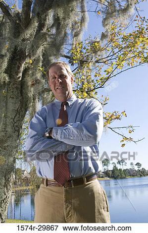 Portrait of a businessman standing with his arms crossed by a tree with the river in the background View Large Photo Image Stock Photo - Portrait of a businessman standing with his arms crossed by a tree with the river in the background. Fotosearch