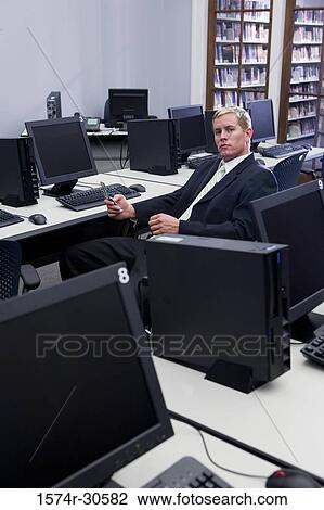 Stock Image - Portrait of a businessman using mobile phone sitting amid computers in an office. Fotosearch