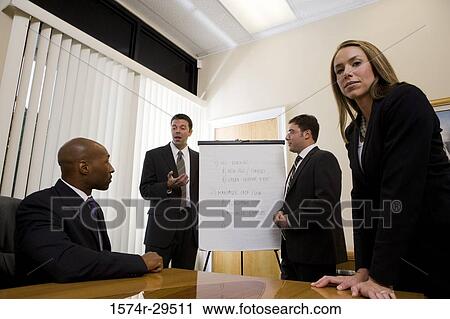 Stock Image - Portrait of a businesswoman standing by table while colleagues in background. Fotosearch