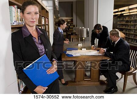 Portrait of a businesswoman standing by wall while colleagues discussing in background View Large Photo Image Stock Image - Portrait of a businesswoman standing by wall while colleagues discussing in background. Fotosearch