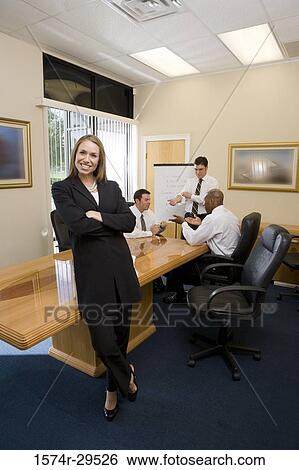 Stock Photograph - Portrait of a businesswoman standing by table with colleagues discussing in background. Fotosearch