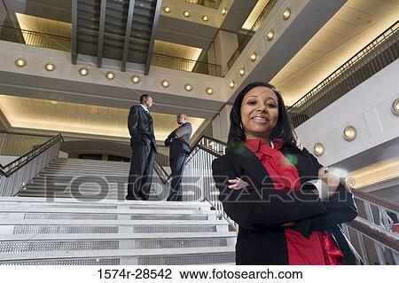 Stock Image - Portrait of a businesswoman standing on staircase while other in the background. Fotosearch