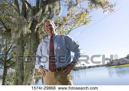 Portrait of a cheerful business man standing with his hand on hip with the river in the background View Large Photo Image Stock Photo - Portrait of a cheerful business man standing with his hand on hip with the river in the background. Fotosearch