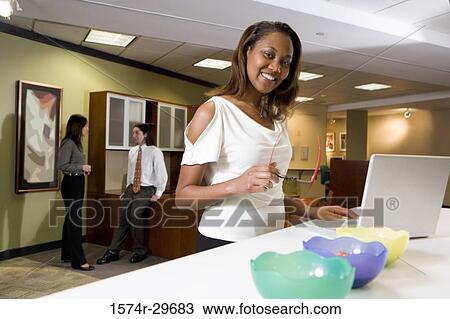 Portrait of a cheerful businesswoman standing in front of a laptop with colleagues discussing in the background View Large Photo Image Stock Image - Portrait of a cheerful businesswoman standing in front of a laptop with colleagues discussing in the background. Fotosearch