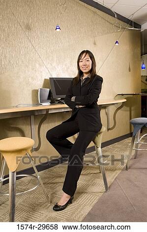 Stock Photo - Portrait of a cheerful businesswoman sitting in office with a computer in the background. Fotosearch