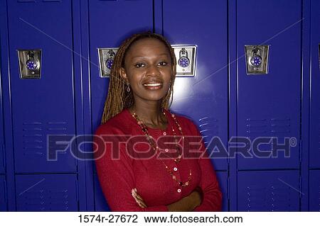 Stock Image - Portrait of a cheerful female teacher standing by locker in corridor. Fotosearch
