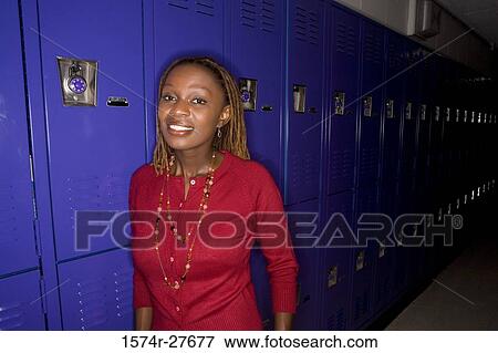 Stock Photo - Portrait of a cheerful female teacher standing by locker in corridor. Fotosearch