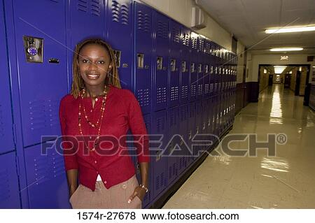 Stock Photo - Portrait of a cheerful female teacher standing by locker in corridor. Fotosearch