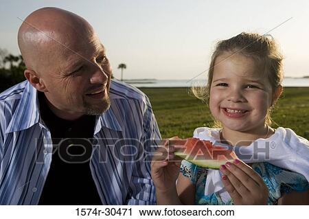 Portrait of a cheerful girl eating watermelon with her father View Large Photo Image Stock Image - Portrait of a cheerful girl eating watermelon with her father. Fotosearch
