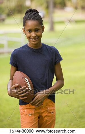 Stock Image - Portrait of a cheerful girl holding a rugby ball at park. Fotosearch