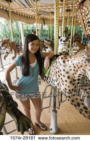 Stock Image - Portrait of a cheerful girl standing in a carousel by a carousel leopard. Fotosearch