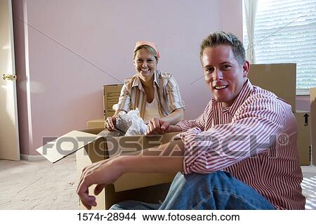 Portrait of a cheerful mid adult couple unpacking cardboard boxes in a house View Large Photo Image Picture - Portrait of a cheerful mid adult couple unpacking cardboard boxes in a house. Fotosearch