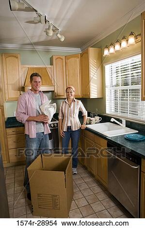 Portrait of a cheerful mid adult couple unpacking cardboard box in the kitchen View Large Photo Image Picture - Portrait of a cheerful mid adult couple unpacking cardboard box in the kitchen. Fotosearch