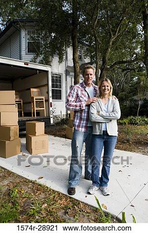 Stock Image - Portrait of a cheerful mid adult couple standing by moving van. Fotosearch