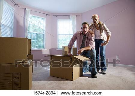 Portrait of a cheerful mid adult couple unpacking cardboard box in a house View Large Photo Image Stock Image - Portrait of a cheerful mid adult couple unpacking cardboard box in a house. Fotosearch