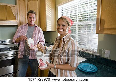 Stock Image - Portrait of a cheerful mid adult couple eating fast food in the kitchen. Fotosearch