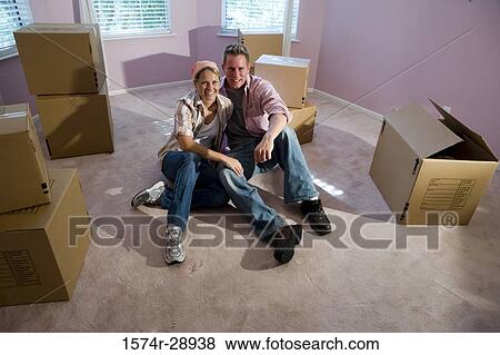 Portrait of a cheerful mid adult couple sitting by cardboard boxes in a house View Large Photo Image Stock Photo - Portrait of a cheerful mid adult couple sitting by cardboard boxes in a house. Fotosearch