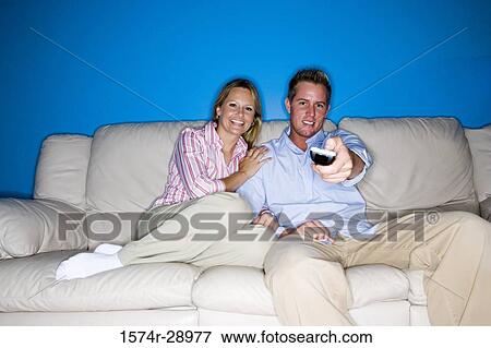 Portrait of a cheerful mid adult couple with remote control sitting on a sofa View Large Photo Image Stock Photo - Portrait of a cheerful mid adult couple with remote control sitting on a sofa. Fotosearch