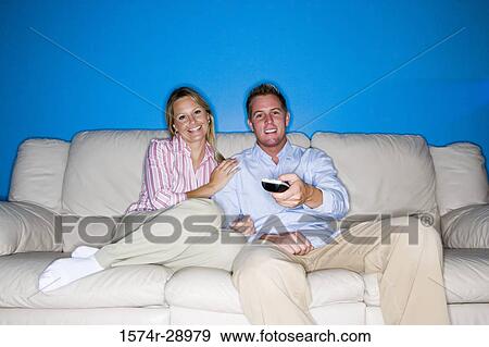 Portrait of a cheerful mid adult couple with remote control sitting on a sofa View Large Photo Image Stock Photo - Portrait of a cheerful mid adult couple with remote control sitting on a sofa. Fotosearch