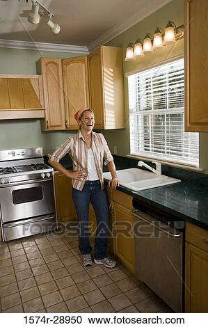 Stock Image - Portrait of a cheerful mid adult woman standing by kitchen counter in the kitchen. Fotosearch