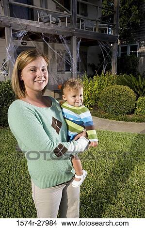 Picture - Portrait of a cheerful mother holding her son in front of a house. Fotosearch