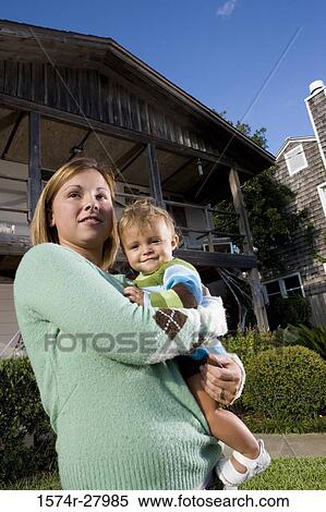 Stock Photography - Portrait of a cheerful mother holding her son in front of a house. Fotosearch