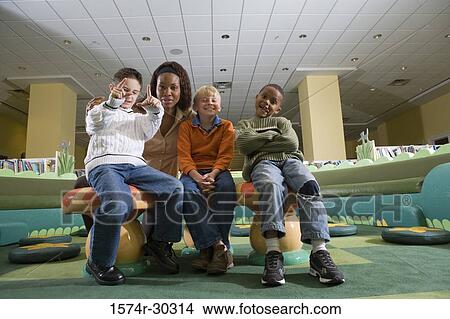 Picture - Portrait of a cheerful teacher sitting with schoolboys in the library. Fotosearch