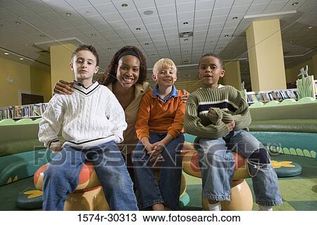 Stock Image - Portrait of a cheerful teacher sitting with schoolboys in the library. Fotosearch