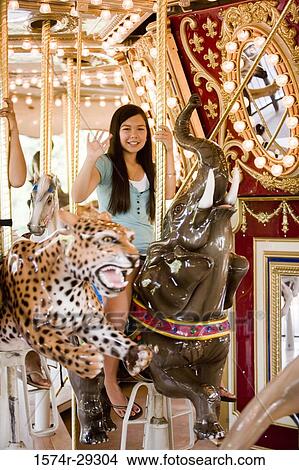Portrait of a cheerful teenage girl sitting on a carousel and waving hand View Large Photo Image Picture - Portrait of a cheerful teenage girl sitting on a carousel and waving hand. Fotosearch