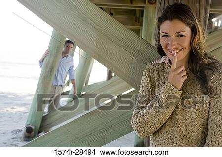 Portrait of a cheerful woman hiding and a man standing in the background View Large Photo Image Picture - Portrait of a cheerful woman hiding and a man standing in the background. Fotosearch