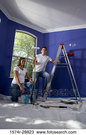 Stock Image - Portrait of a cheerful young couple with step ladder and paint roller in house. Fotosearch