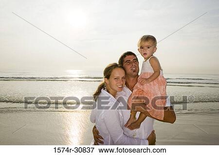 Stock Photo - Portrait of a cheerful young couple with their daughter on the beach. Fotosearch