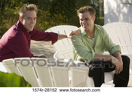 Portrait of a cheerful young man sitting on armchairs with hand on shoulder to other View Large Photo Image Stock Image - Portrait of a cheerful young man sitting on armchairs with hand on shoulder to other. Fotosearch
