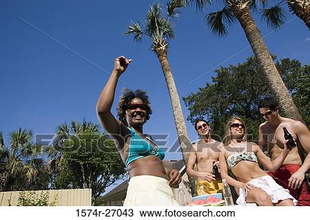 Stock Image - Portrait of a cheerful young woman standing with arms raised while her friends in the background. Fotosearch