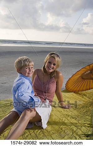 Stock Image - Portrait of a cheerful young woman sitting with her son at the beach. Fotosearch