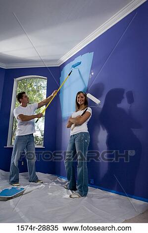 Portrait of a cheerful young woman holding paint roller with arms crossed and young man painting wall View Large Photo Image Stock Photography - Portrait of a cheerful young woman holding paint roller with arms crossed and young man painting wall. Fotosearch