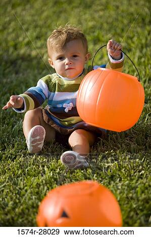 Stock Photo - Portrait of a cute boy holding pumpkin Halloween bag on grass. Fotosearch