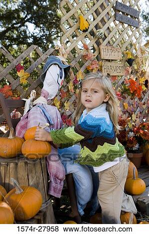 Stock Photo - Portrait of a cute girl in warm clothing standing by scarecrow. Fotosearch