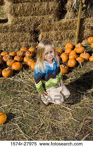 Stock Photography - Portrait of a cute girl in warm clothing kneeling by pumpkins. Fotosearch