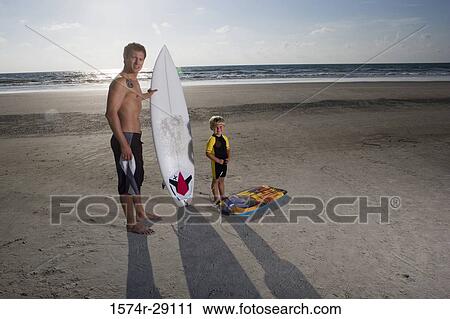 Portrait of a father with his son standing by surfboard at the beach View Large Photo Image Stock Image - Portrait of a father with his son standing by surfboard at the beach. Fotosearch