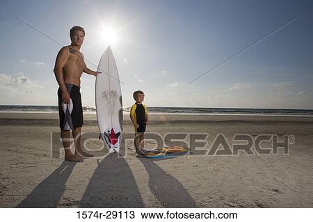 Portrait of a father with his son standing by surfboard at the beach View Large Photo Image Stock Image - Portrait of a father with his son standing by surfboard at the beach. Fotosearch